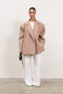 Woman wearing a beige blazer and white pants against a plain background