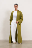 Woman wearing a long green cardigan over a white top and pants on a plain background