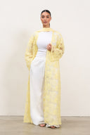 Woman wearing a yellow lace cardigan over a white outfit on a plain background