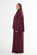 Woman wearing a burgundy abaya and hijab on a white background
