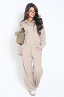 Woman wearing a taupe knit V-neck polo sweater with matching wide-leg knit pants; relaxed, cozy fit.
